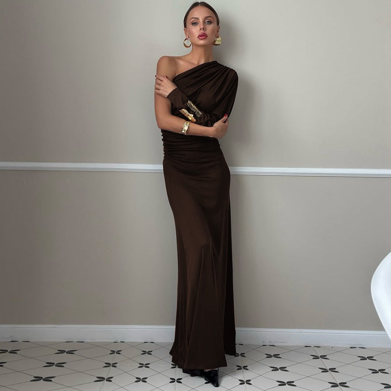Woman in a brown evening gown standing against a plain wall.