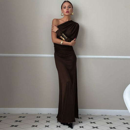 Woman in a brown evening gown standing against a plain wall.